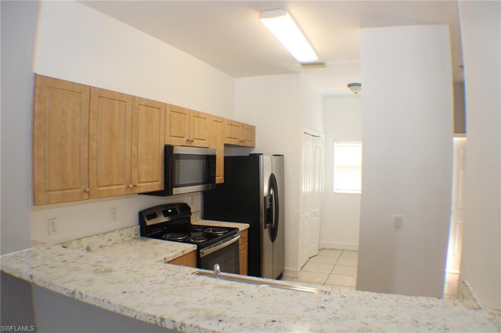 Kitchen featuring stainless steel appliances, light tile patterned floors, light stone countertops, light brown cabinetry, and a peninsula