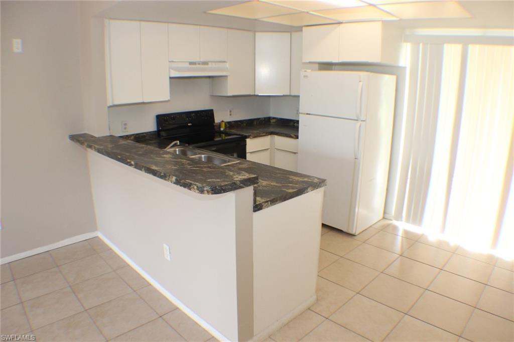 Kitchen with freestanding refrigerator, light tile patterned flooring, black range with electric stovetop, and white cabinetry