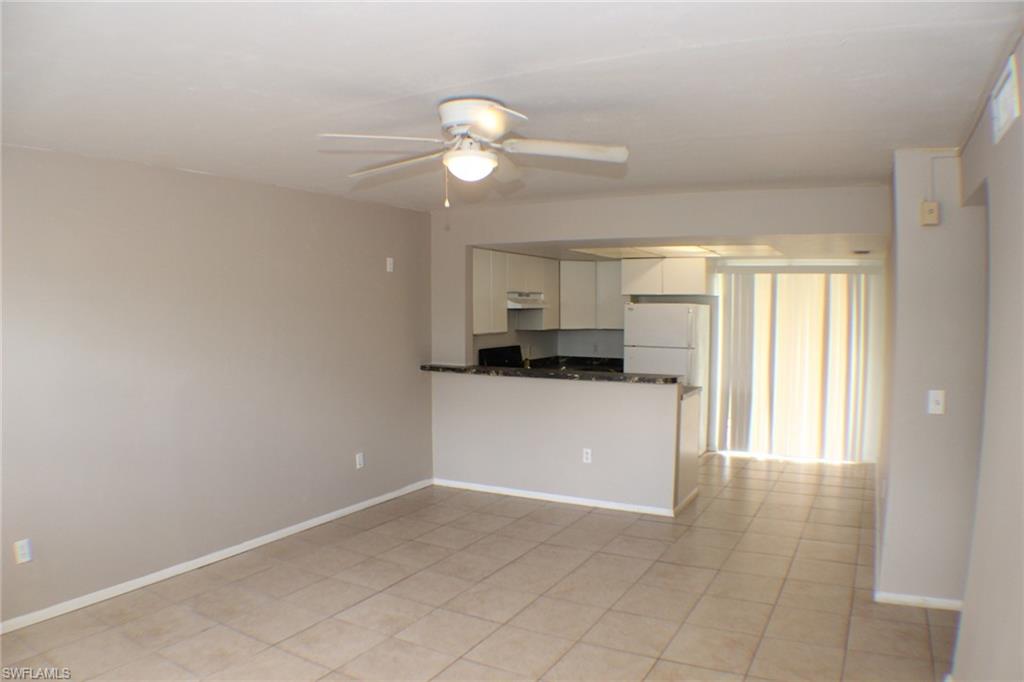 Kitchen with a ceiling fan, freestanding refrigerator, a peninsula, light tile patterned floors, and under cabinet range hood