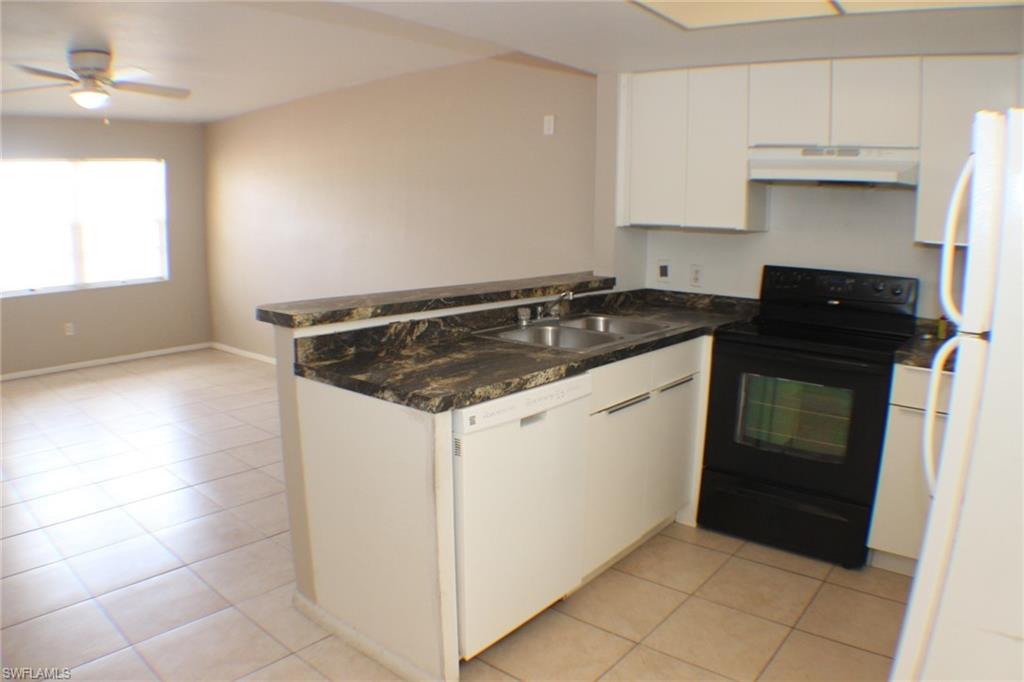 Kitchen with white appliances, white cabinets, light tile patterned flooring, and dark countertops
