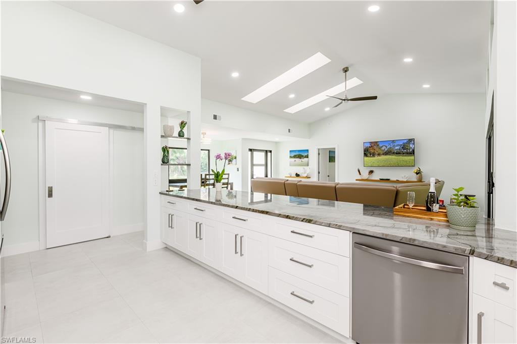 Kitchen featuring stone countertops, white cabinetry, stainless steel dishwasher, vaulted ceiling, and recessed lighting