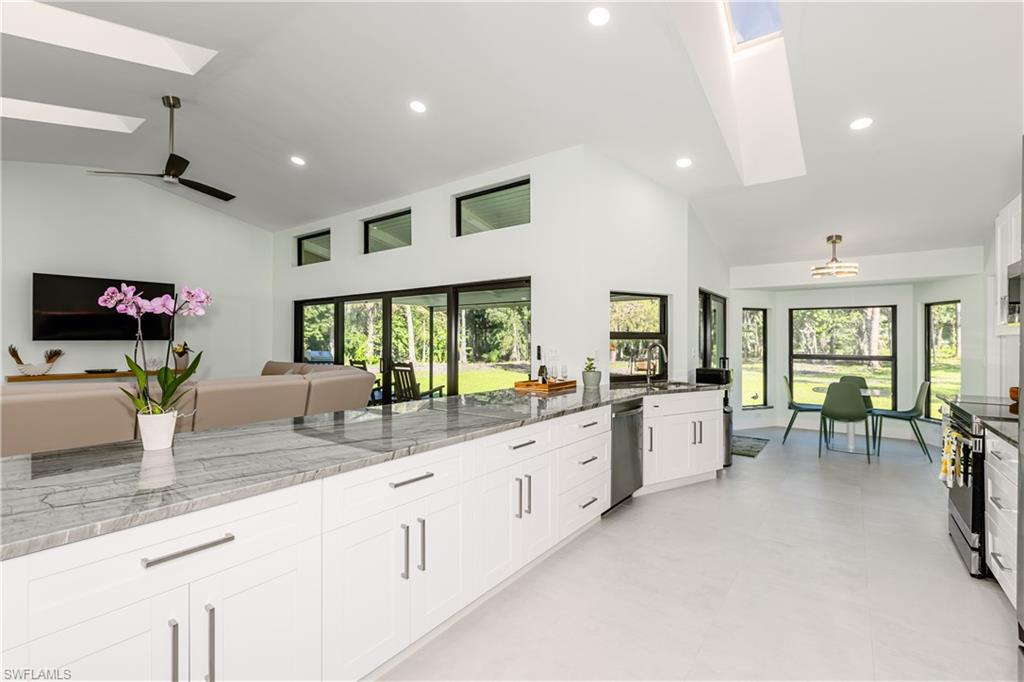 Open floor plan with Vaulted ceilings, skylights, white cabinetry, quartzite stone counters, and recessed lighting