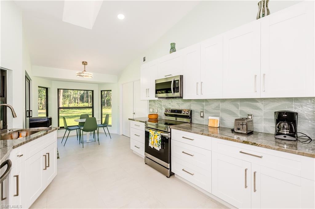 Kitchen featuring stainless steel appliances, backsplash, white cabinetry, light stone counters, and recessed lighting