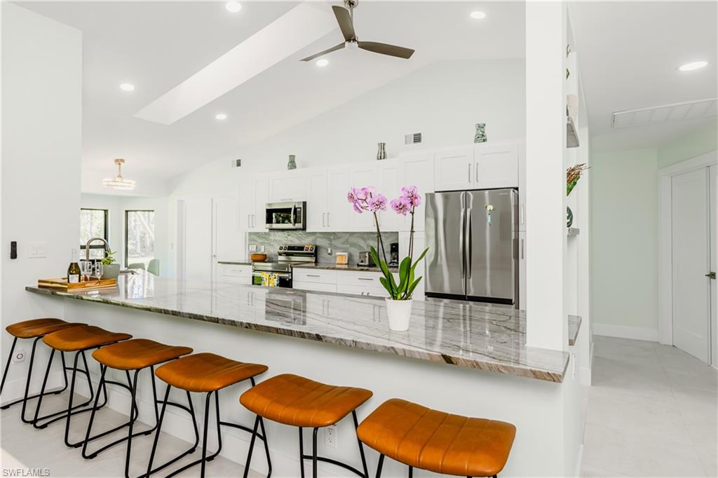 Kitchen with a peninsula, backsplash, appliances with stainless steel finishes, lofted ceiling, and white cabinetry