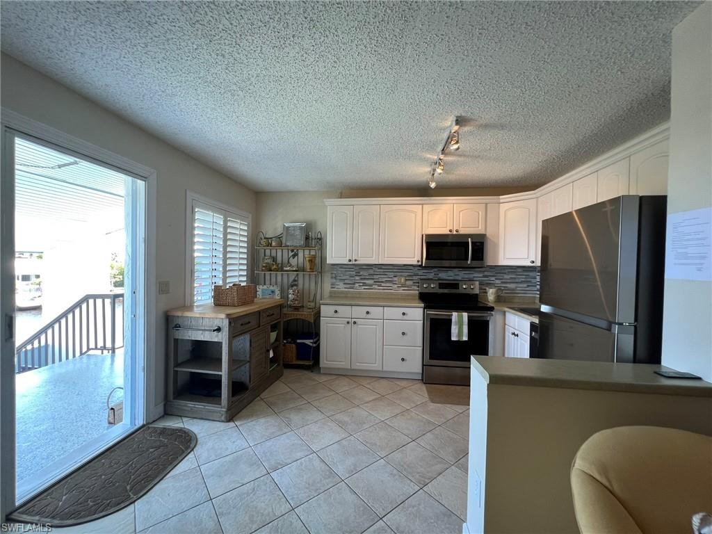 Kitchen with stainless steel appliances, decorative backsplash, white cabinets, a textured ceiling, and light tile patterned flooring