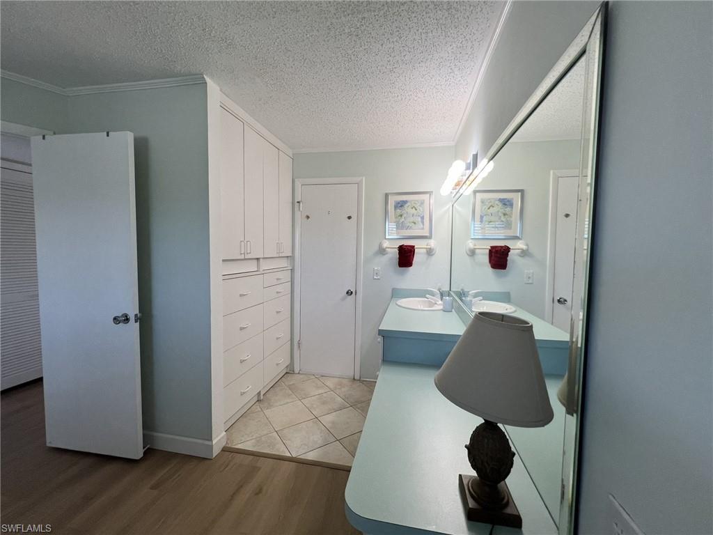 Full bathroom featuring light wood-type flooring, vanity, a textured ceiling, and crown molding