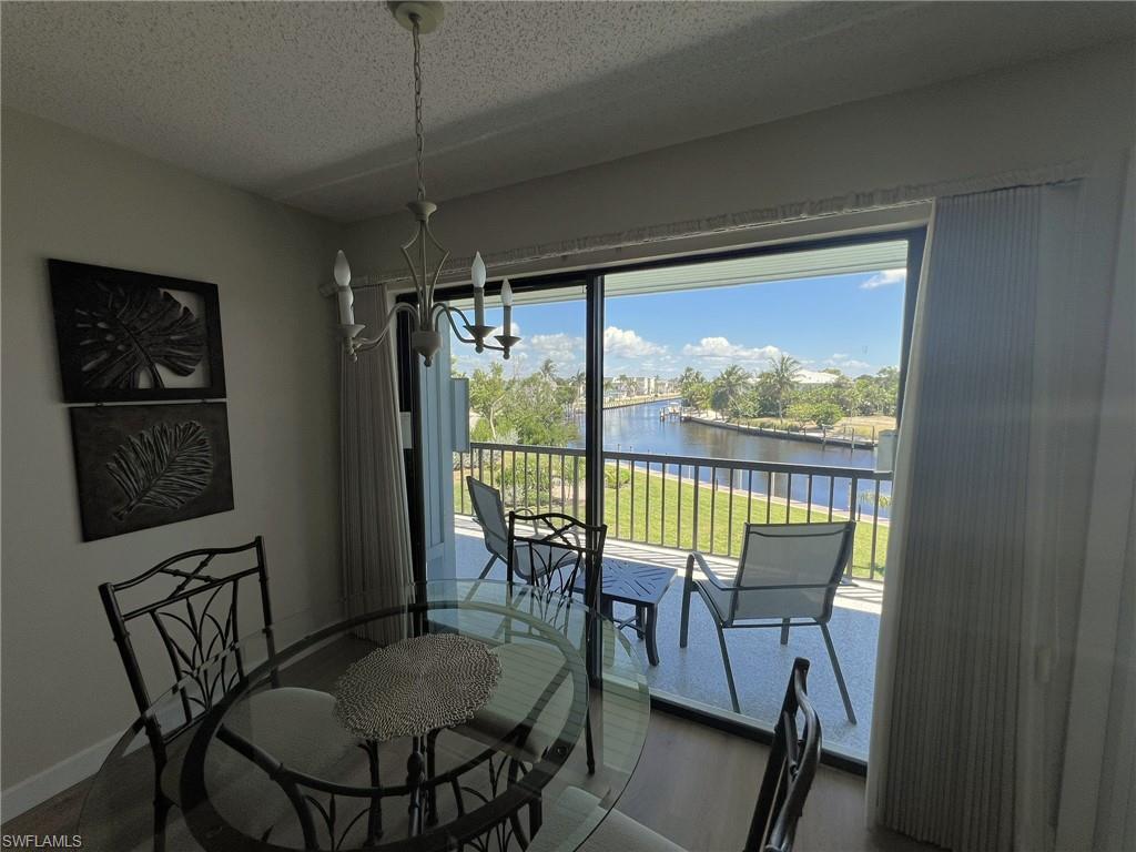 Dining space with a water view, a textured ceiling, wood finished floors, and a chandelier