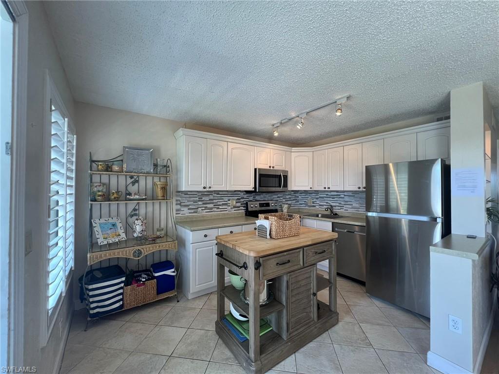 Kitchen featuring stainless steel appliances, light tile patterned flooring, light countertops, decorative backsplash, and a textured ceiling