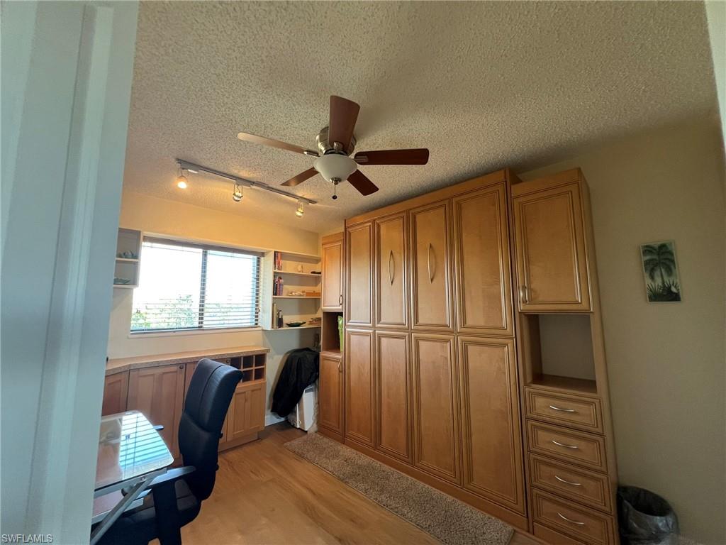 Office space featuring a textured ceiling, rail lighting, light wood-type flooring, and ceiling fan