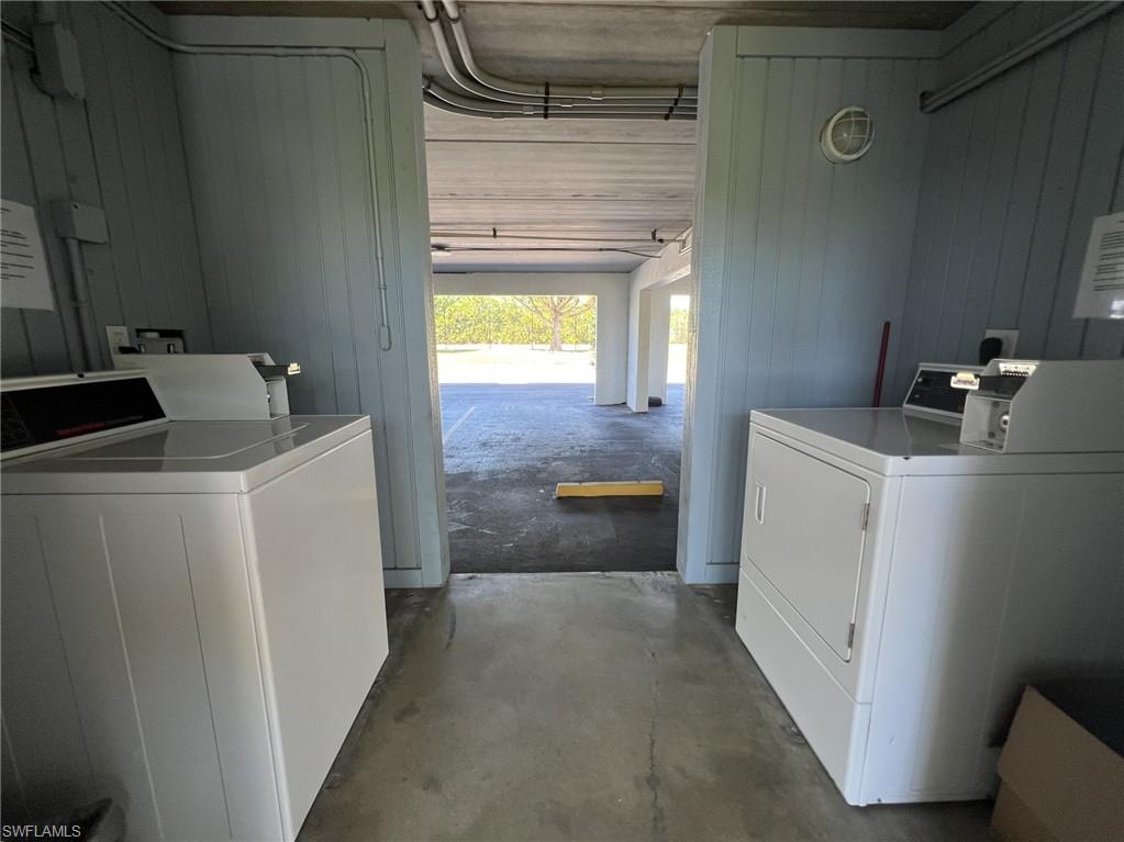 Shared laundry room with unfinished concrete flooring, independent washer and dryer, a garage, and wood walls