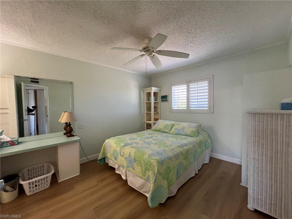 Bedroom featuring crown molding, dark wood-type flooring, a textured ceiling, and ceiling fan