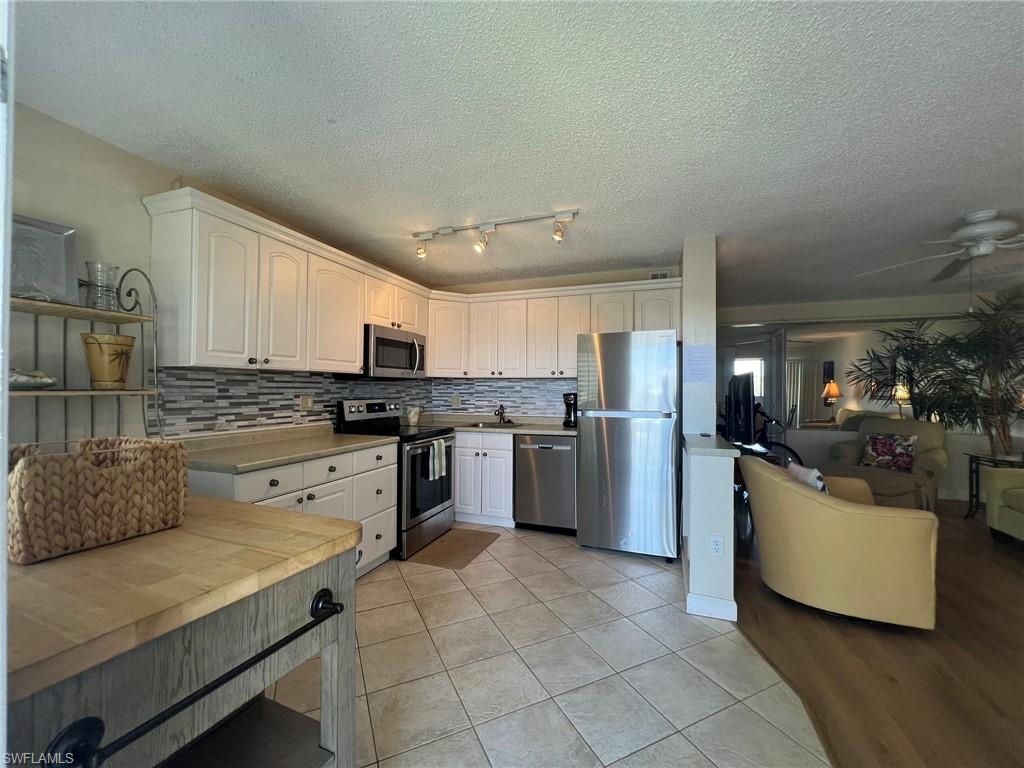 Kitchen featuring stainless steel appliances, a textured ceiling, tasteful backsplash, white cabinetry, and light tile patterned floors