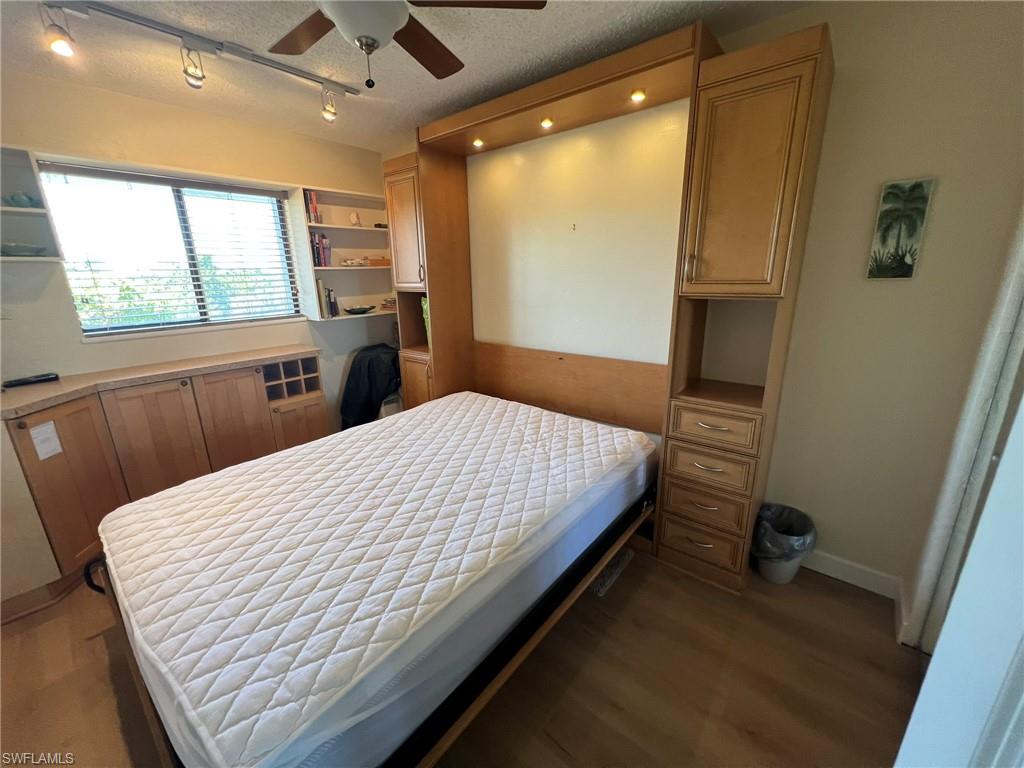 Bedroom with a textured ceiling, dark wood-style flooring, rail lighting, and a ceiling fan