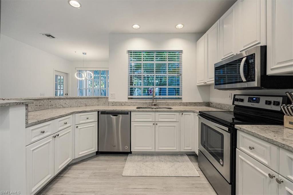 Kitchen with stainless steel appliances, white cabinets, light stone counters, recessed lighting, and decorative light fixtures
