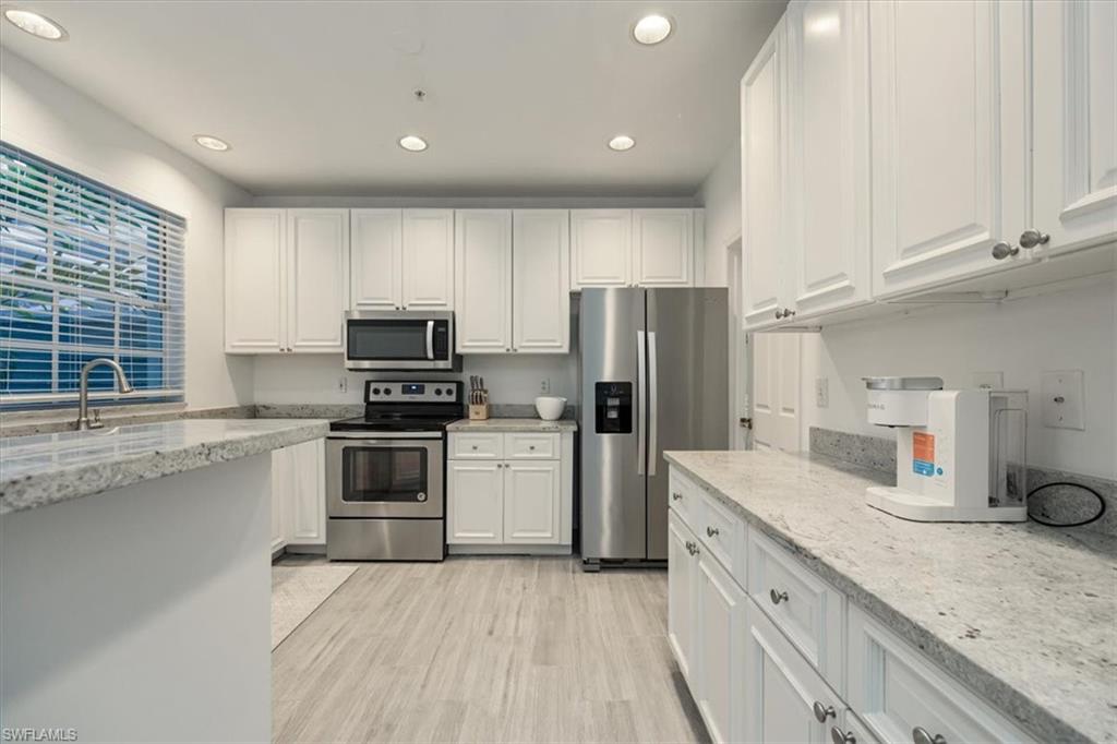 Kitchen with stainless steel appliances, white cabinets, light stone countertops, recessed lighting, and light wood finished floors
