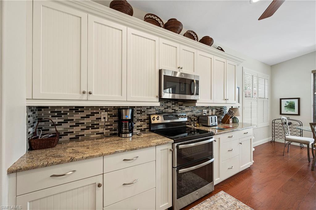 Kitchen with stainless steel appliances, tasteful backsplash, light stone counters, white cabinetry, and dark wood-type flooring