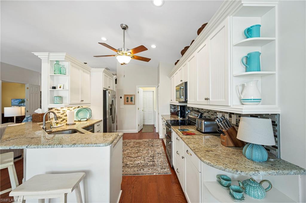 Kitchen with open shelves, decorative backsplash, dark wood finished floors, light stone countertops, and a peninsula