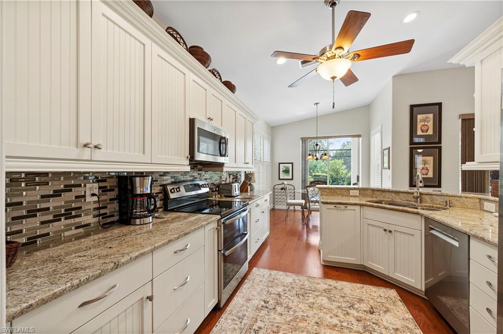 Kitchen featuring appliances with stainless steel finishes, decorative backsplash, dark wood-type flooring, light stone counters, and vaulted ceiling