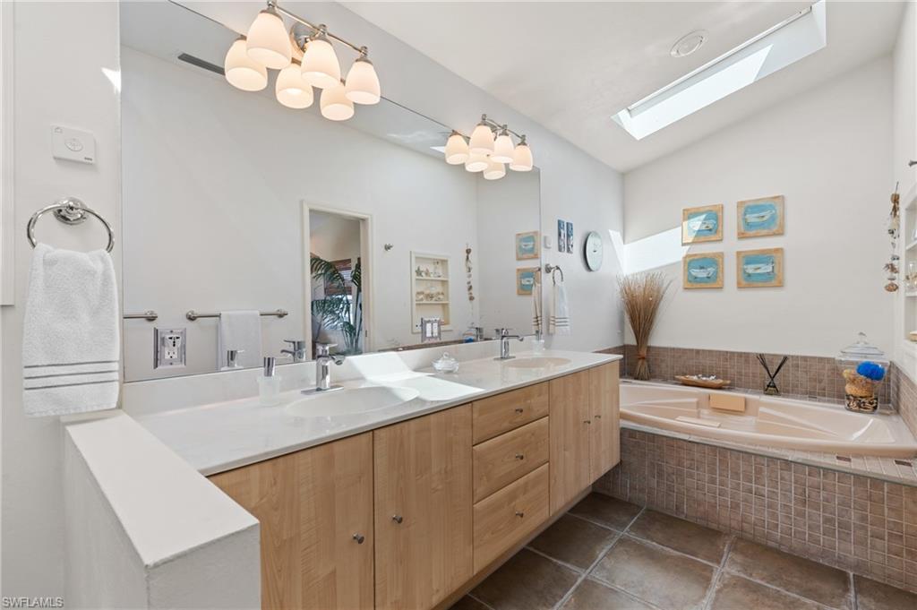 Bathroom featuring vanity, tile patterned floors, tiled bath, and vaulted ceiling with skylight
