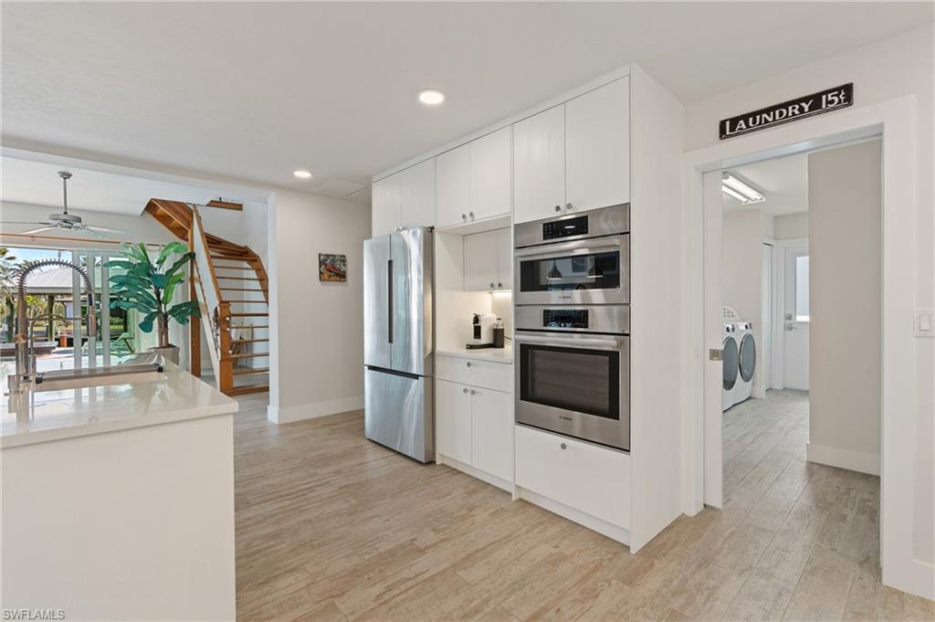 Kitchen with stainless steel appliances, white cabinets, independent washer and dryer, and light wood look tile flooring