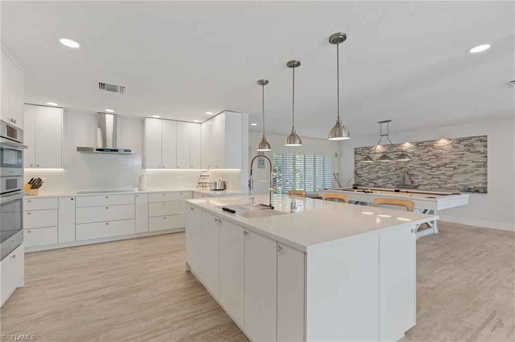 Kitchen with exhaust hood, sink, white cabinetry, pendant lighting, and a large island