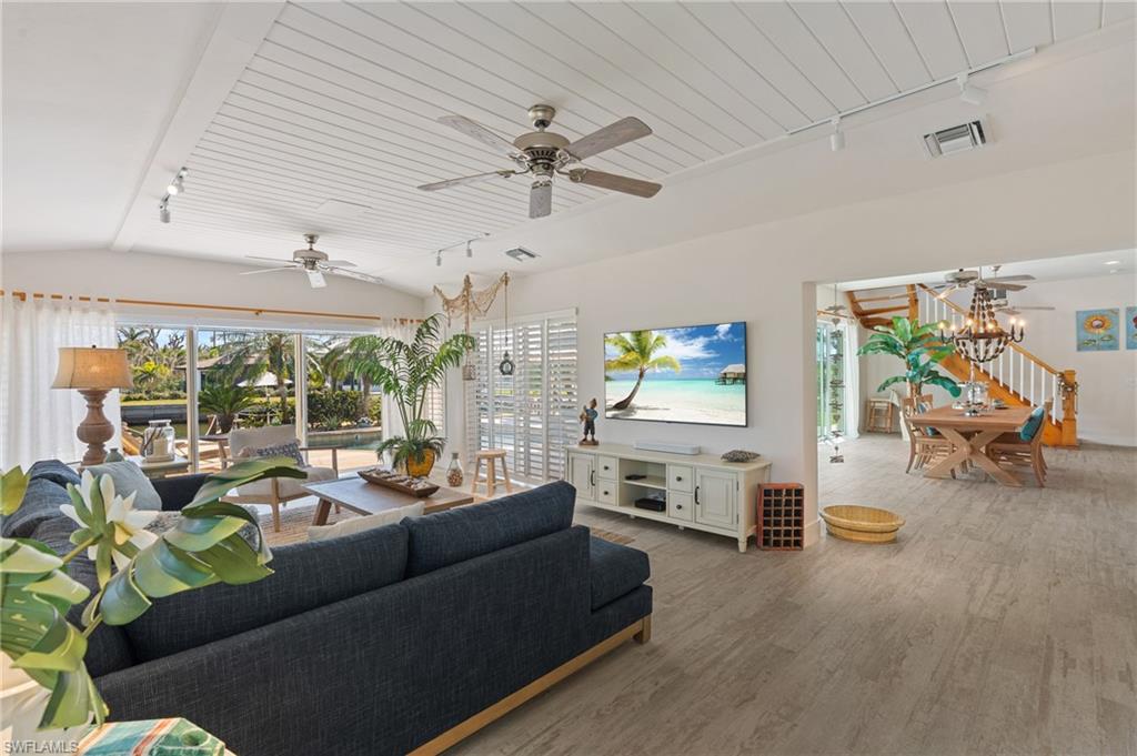 Living room featuring wood look tile floors, ceiling fan with notable chandelier, vaulted ceiling, and rail lighting