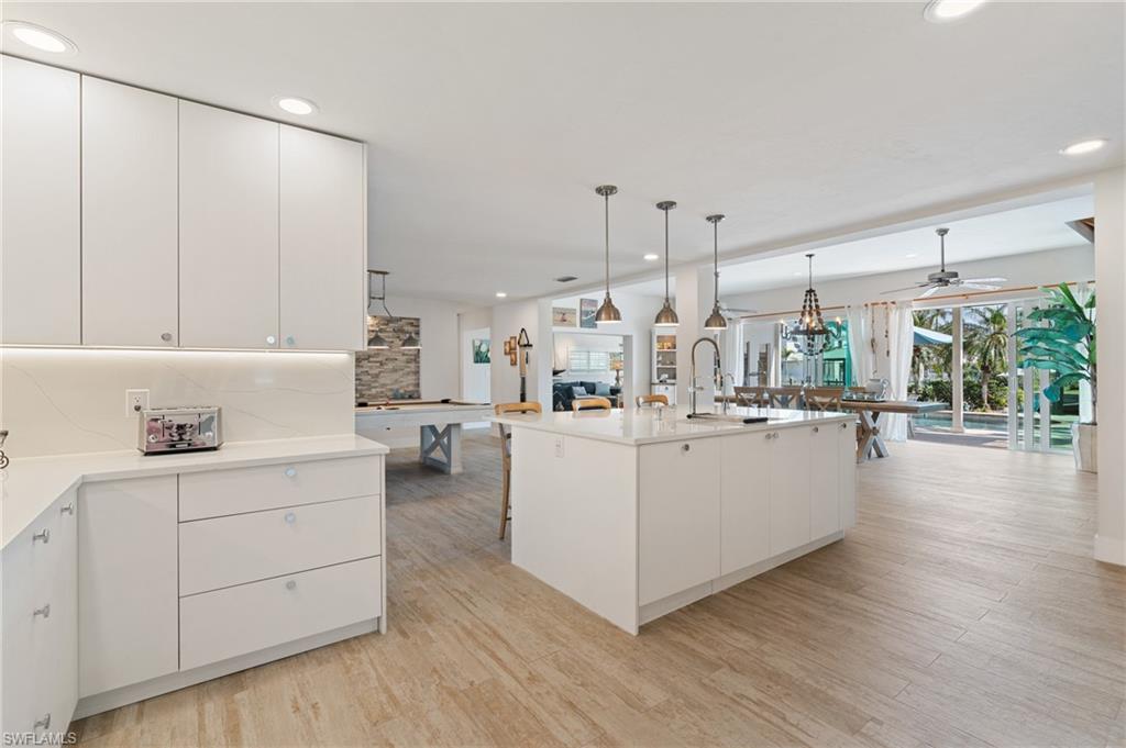 Kitchen with decorative light fixtures, wood look tile flooring, an island with sink, decorative backsplash, and white cabinets