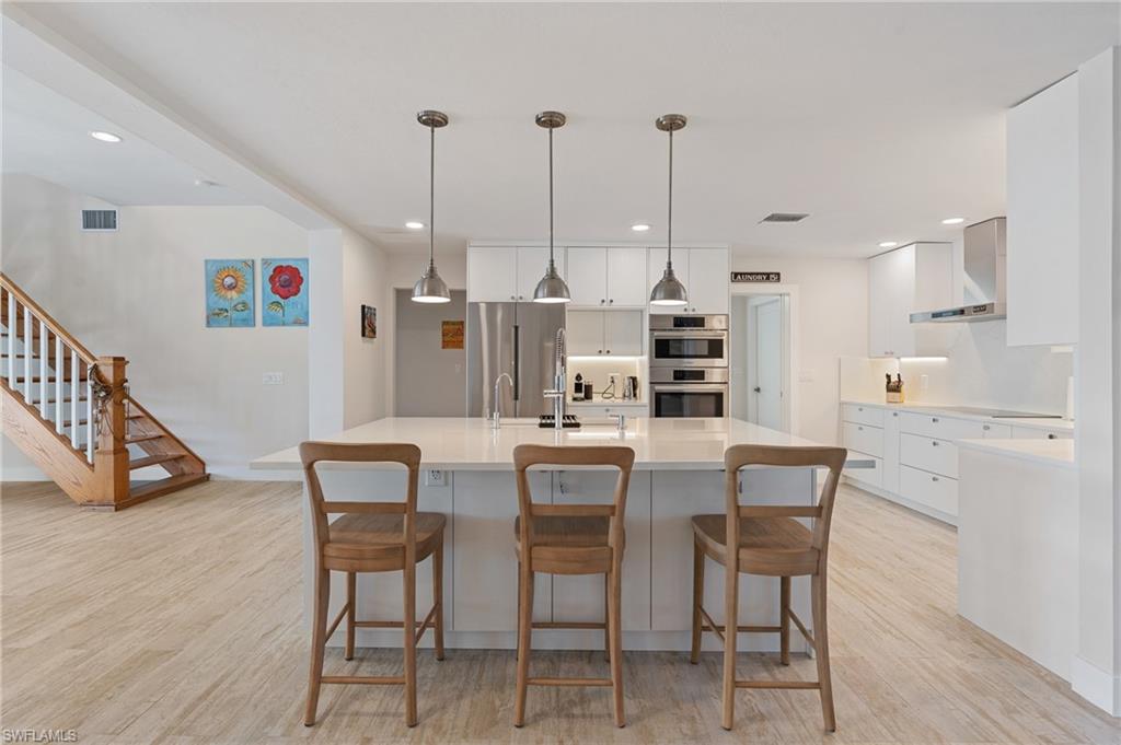 Kitchen featuring a spacious island,  exhaust hood, white cabinetry, hanging light fixtures, and appliances with stainless steel finishes