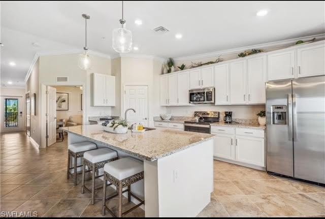 Kitchen with appliances with stainless steel finishes, crown molding, white cabinets, a breakfast bar area, and hanging light fixtures