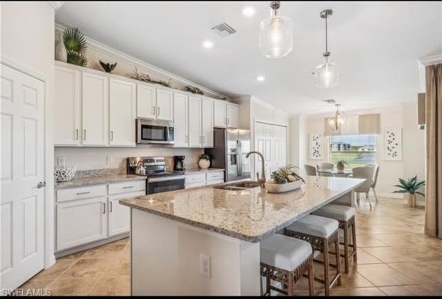 Kitchen featuring a breakfast bar, white cabinets, pendant lighting, stainless steel appliances, and ornamental molding