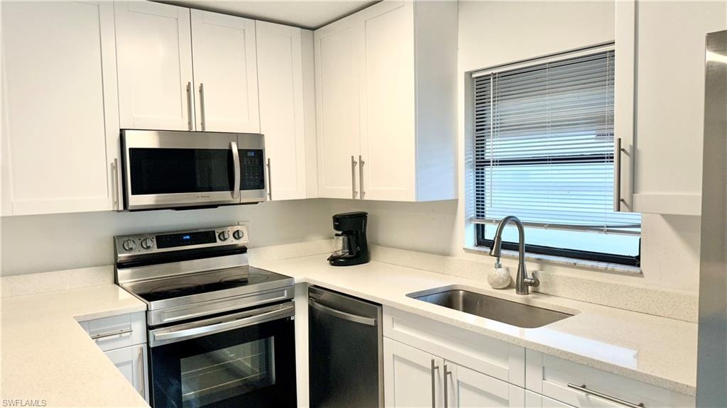 Kitchen featuring appliances with stainless steel finishes, white cabinetry, and light stone counters