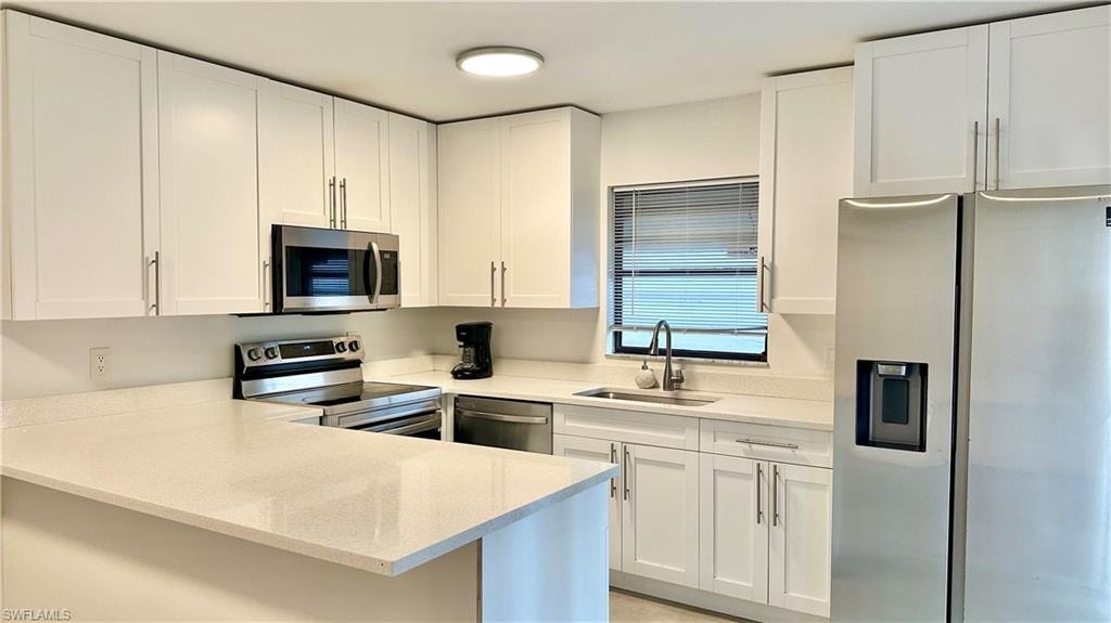 Kitchen featuring appliances with stainless steel finishes, light stone counters, a peninsula, and white cabinetry