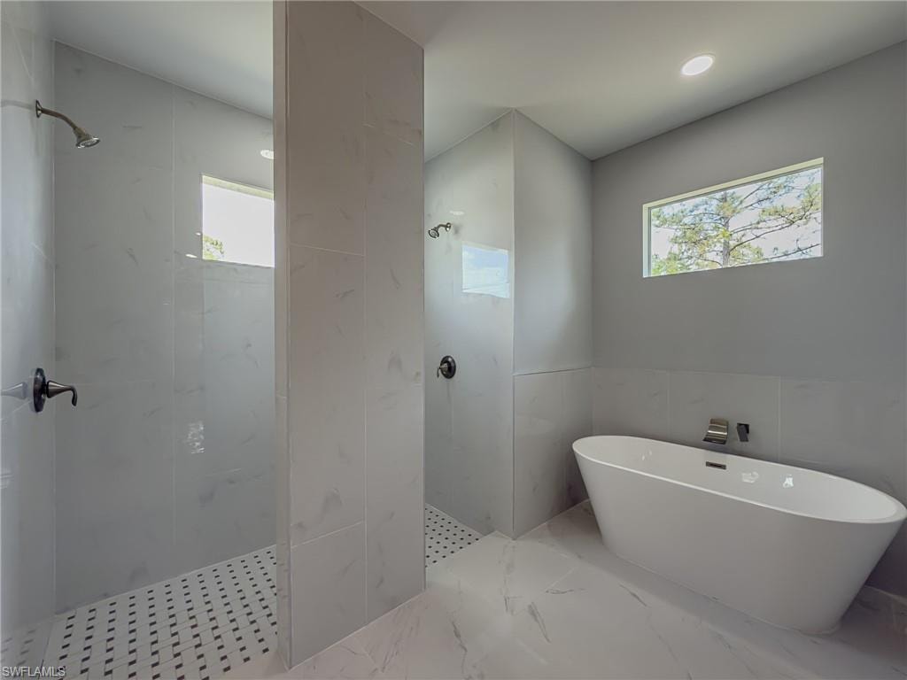 Bathroom featuring walk in shower, tile walls, a freestanding tub, and marble finish floor