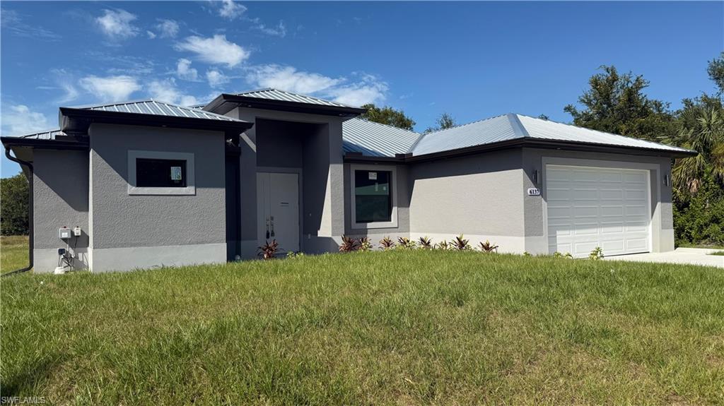View of front of property featuring an attached garage, stucco siding, a front yard, and a metal roof