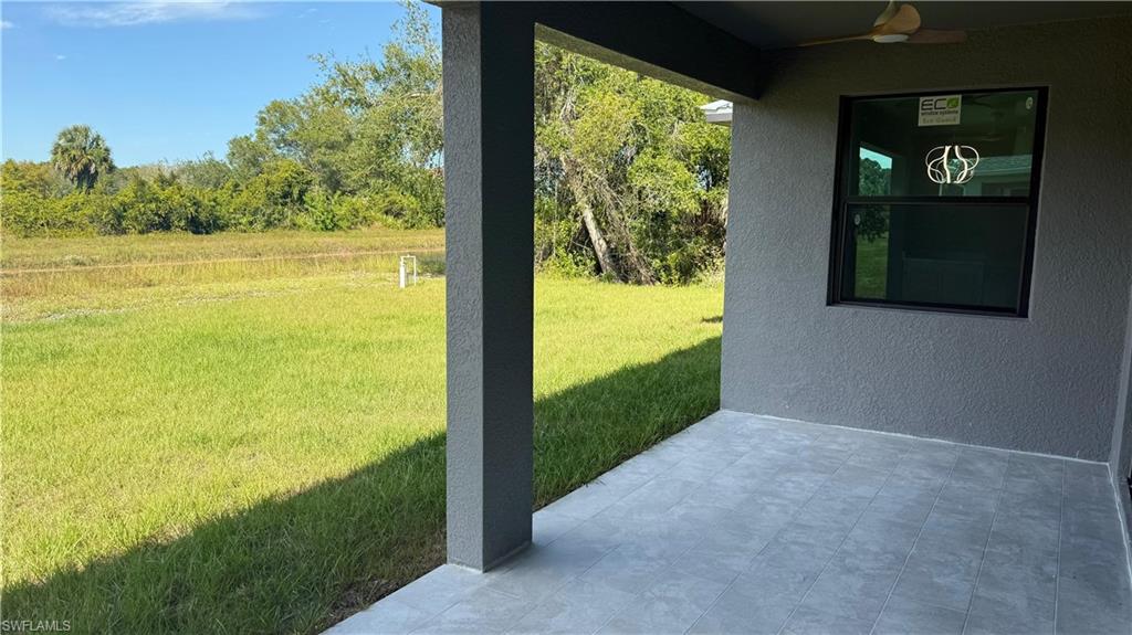 View of green lawn with a patio and ceiling fan