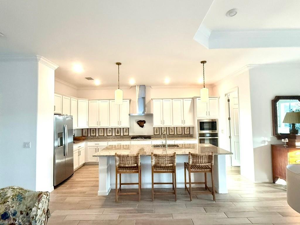 Kitchen featuring a breakfast bar, an island with sink, appliances with stainless steel finishes, light stone countertops, and crown molding