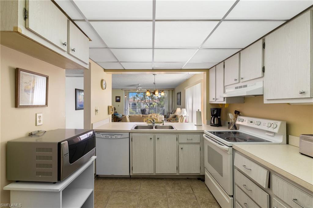 Kitchen featuring white appliances, light countertops, decorative light fixtures, under cabinet range hood, and light tile patterned floors