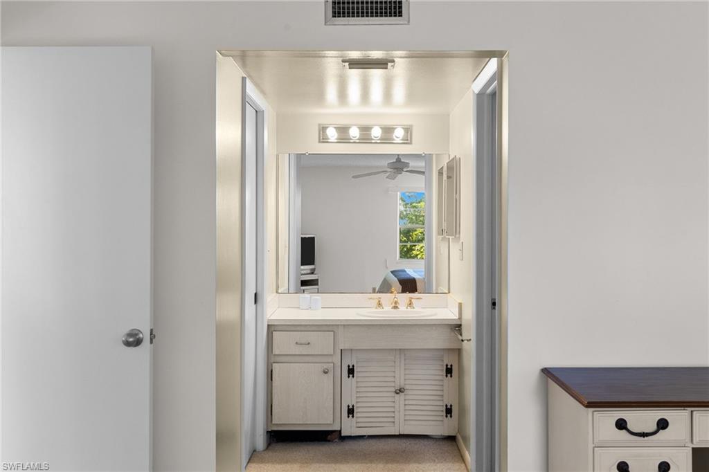 Ensuite bathroom featuring vanity, light colored carpet, and ceiling fan