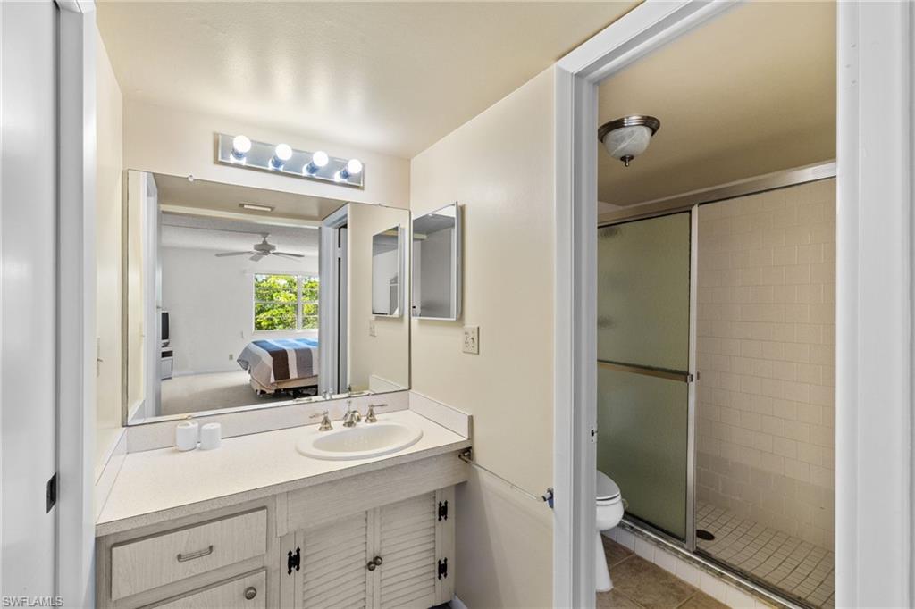 Bathroom featuring connected bathroom, vanity, a stall shower, light tile patterned flooring, and ceiling fan