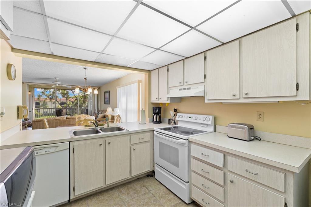 Kitchen featuring white appliances, light countertops, under cabinet range hood, pendant lighting, and open floor plan