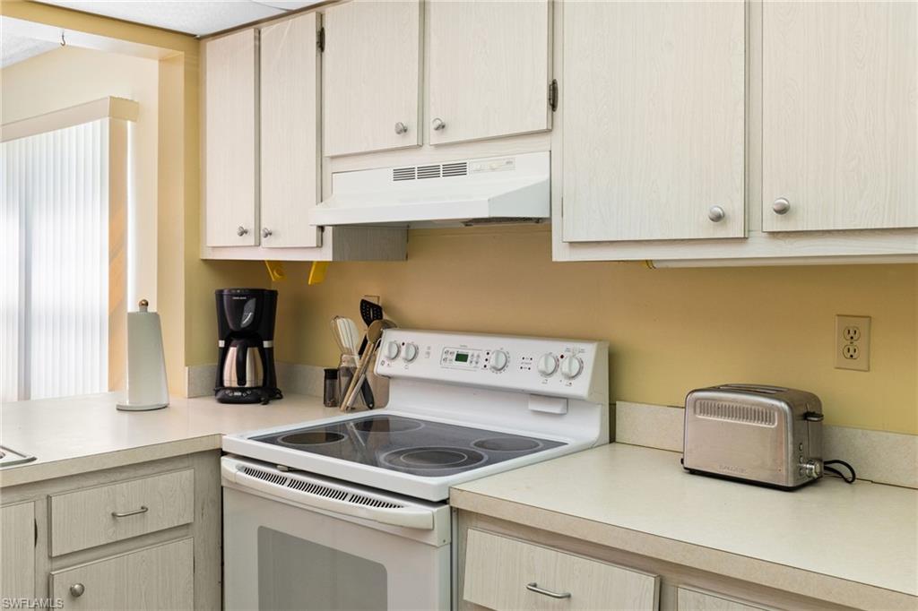 Kitchen with white range with electric cooktop, light countertops, under cabinet range hood, and light brown cabinetry