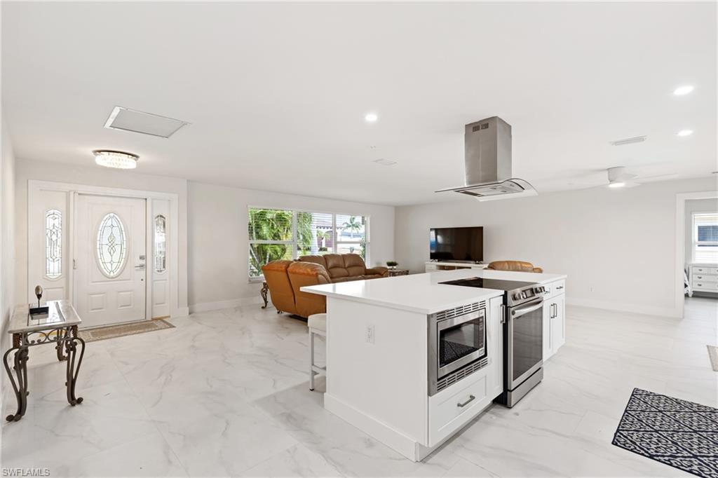 Kitchen featuring light marble finish floors, a center island, open floor plan, island range hood, and recessed lighting