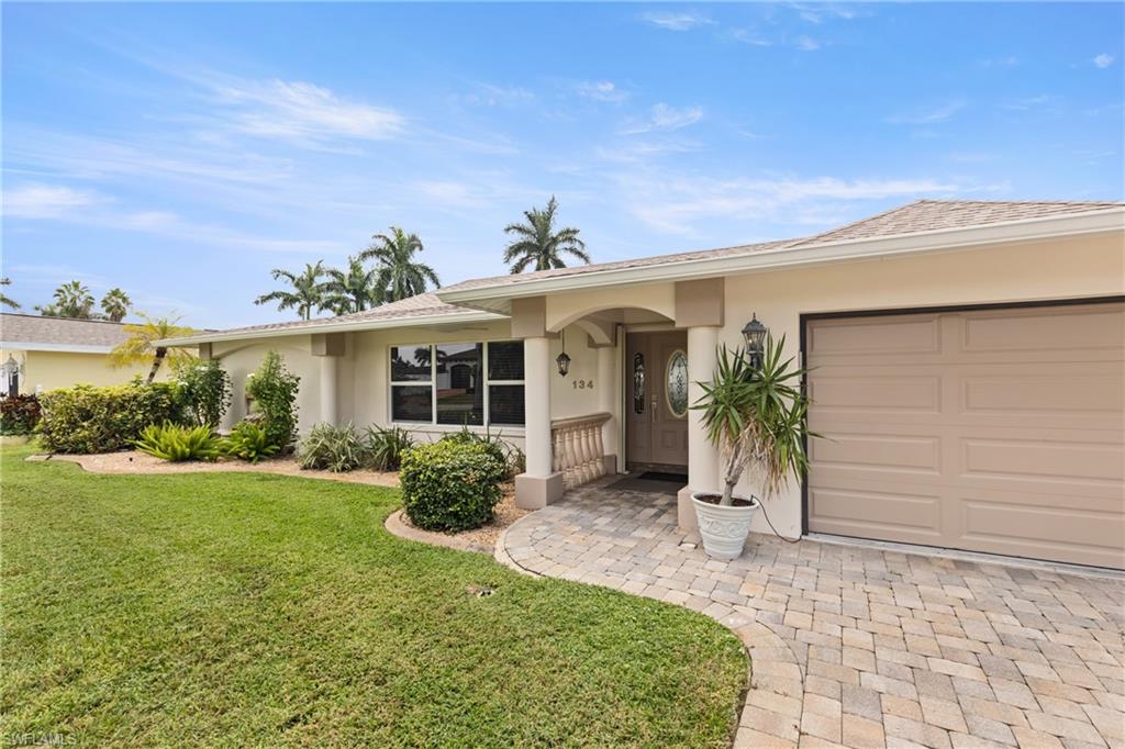 Ranch-style home with stucco siding, a front yard, an attached garage, and decorative driveway