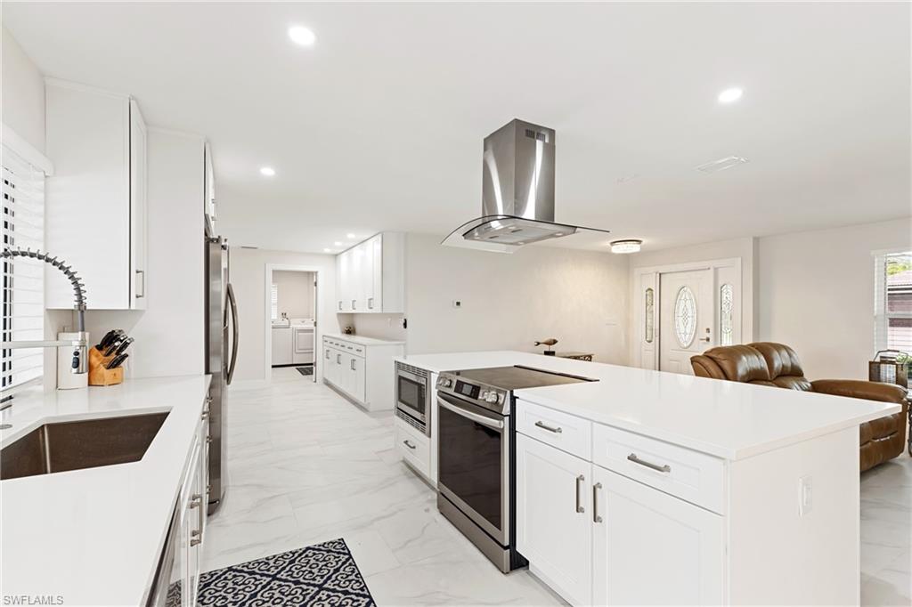 Kitchen featuring appliances with stainless steel finishes, white cabinets, island exhaust hood, light marble finish floors, and recessed lighting