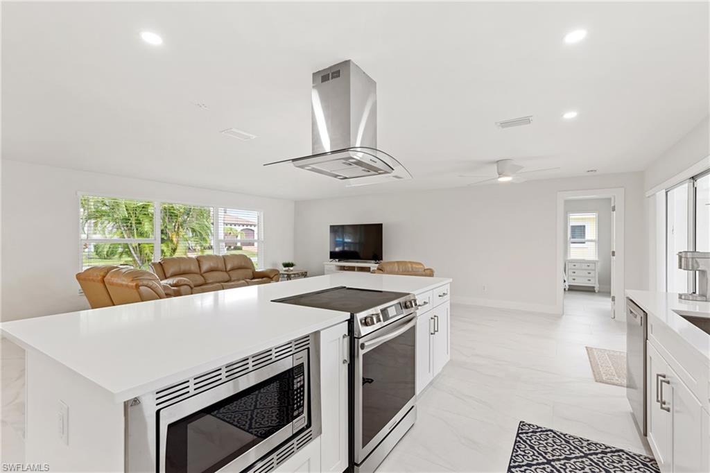 Kitchen with stainless steel appliances, recessed lighting, island exhaust hood, white cabinetry, and open floor plan