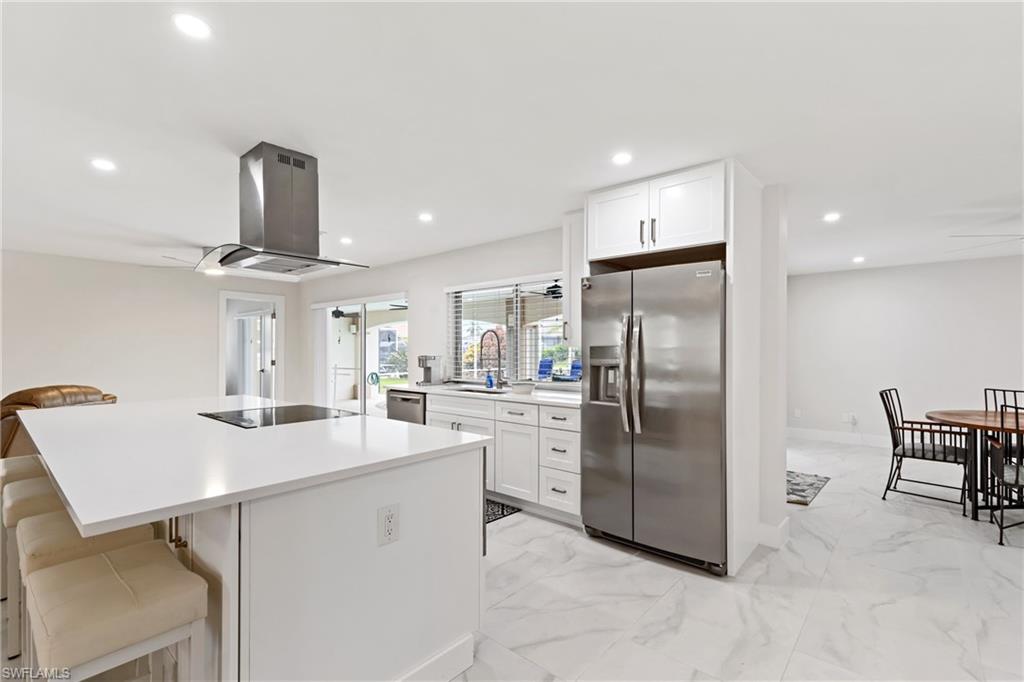 Kitchen with appliances with stainless steel finishes, white cabinets, a breakfast bar, light marble finish floors, and recessed lighting