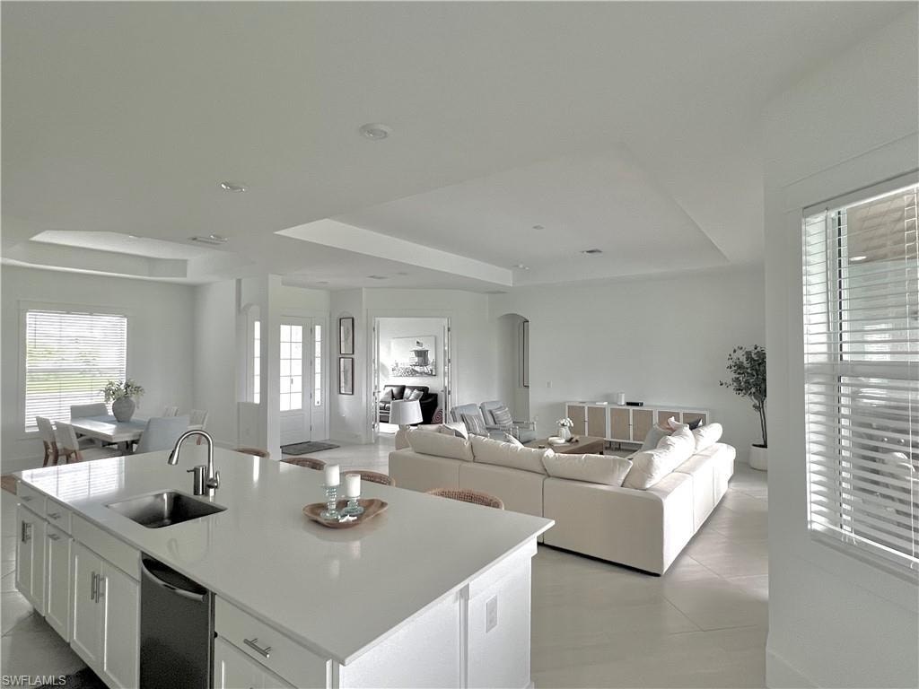 Kitchen with white cabinets, a center island with sink, a raised ceiling, light tile patterned flooring, and sink