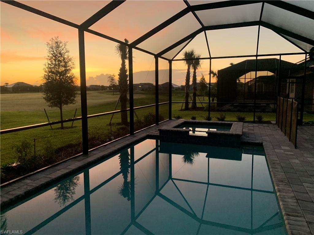 Pool at dusk featuring a patio, an in ground hot tub, a lawn, and a lanai