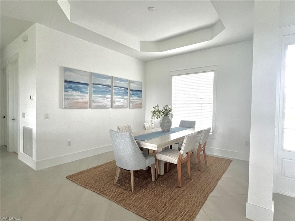 Dining area with light tile patterned floors and a raised ceiling