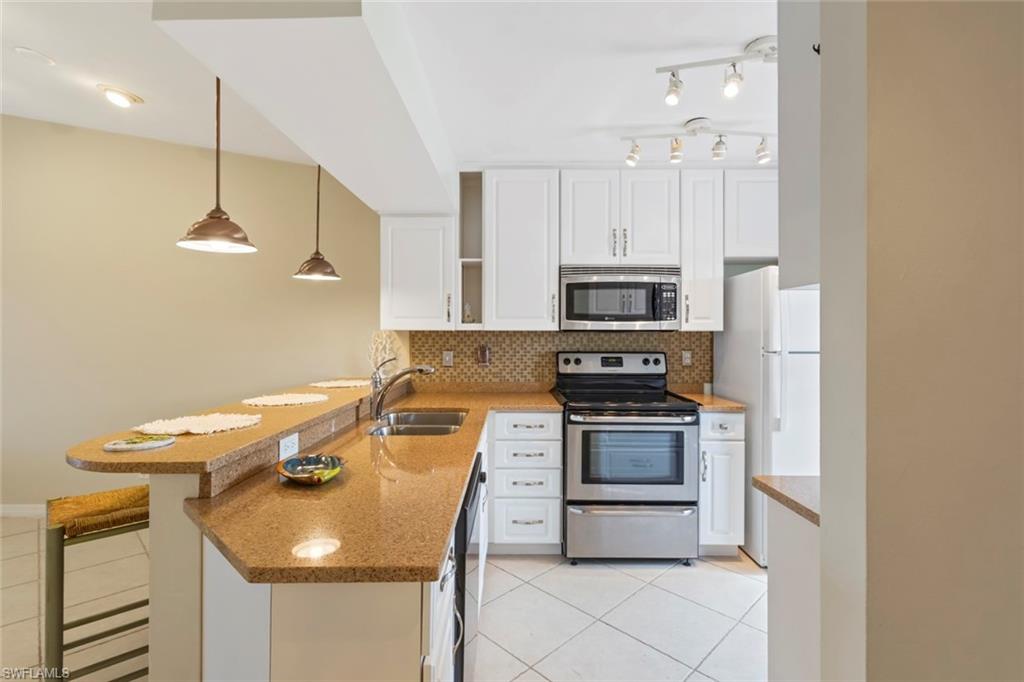 Kitchen featuring light tile patterned floors, white cabinets, stainless steel appliances, hanging light fixtures, and tasteful backsplash